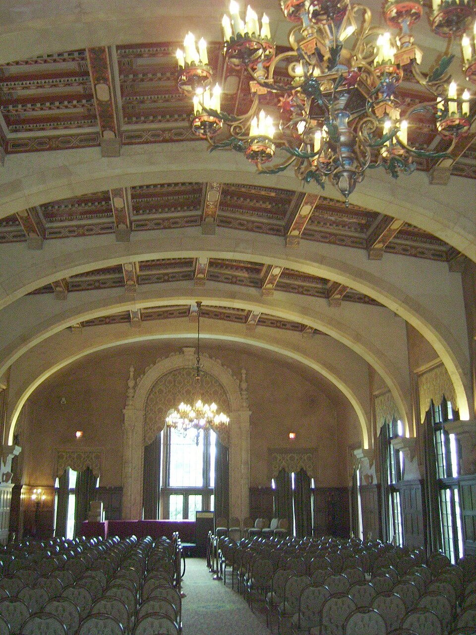 Chandeliers hang beneath a painted ceiling above rows of chairs in the Biltmore Hotel’s arched hall