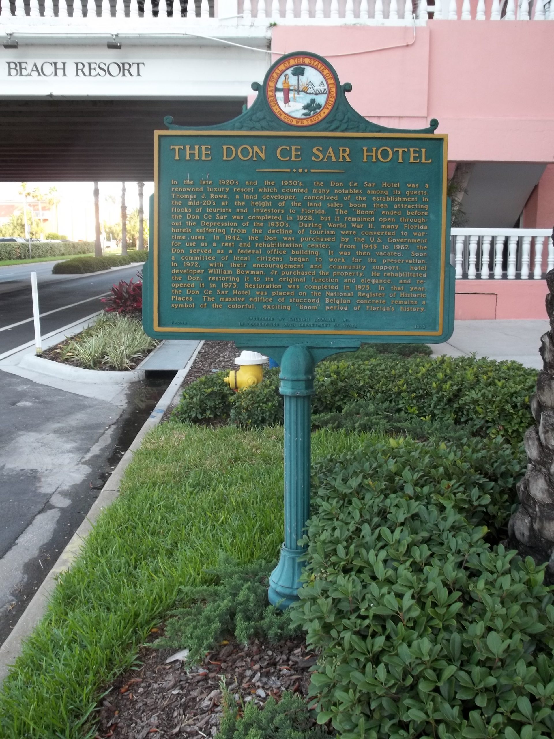 Green historical marker titled The Don Ce Sar Hotel beside the pink exterior and an entrance ramp