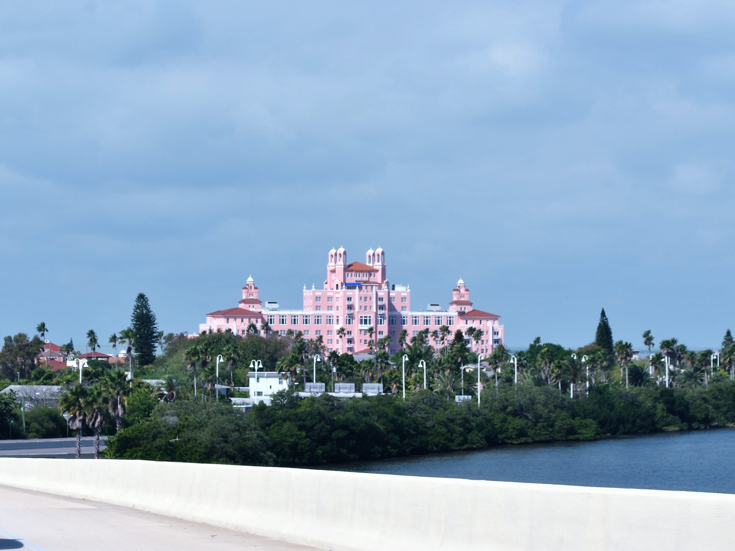The Don CeSar’s pink towers rising beyond water, trees and neighbouring houses, viewed from a bridge